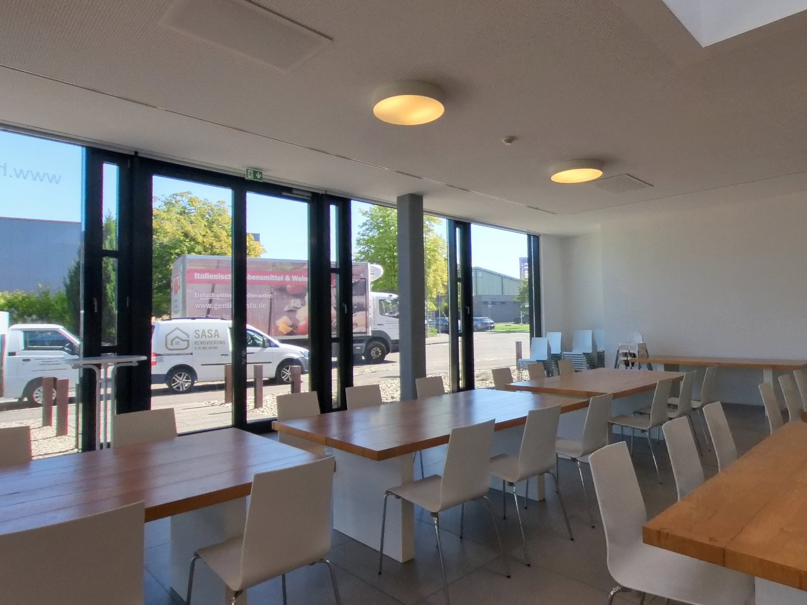 Blick in den Saal zur Glasfront, mit langen Tafeln