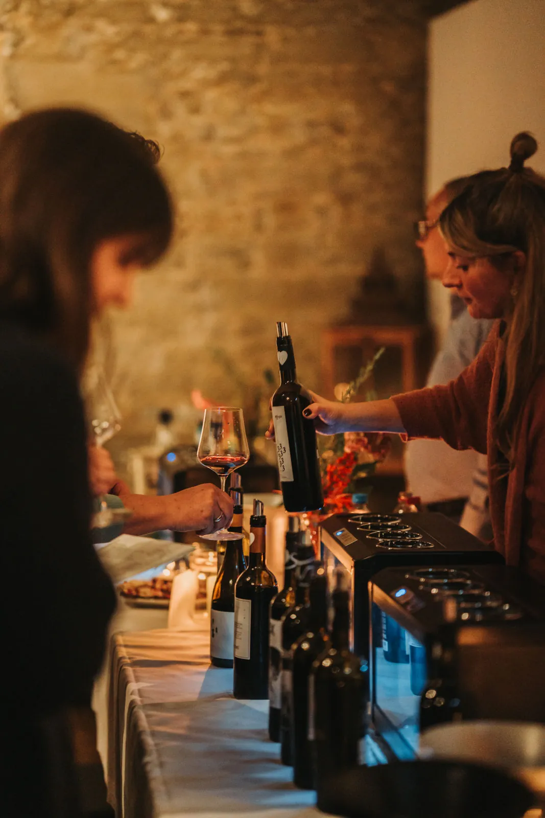 Jessi schenkt bei einer Weinprobe Rotwein aus, im Vordergrund Gläser und Kerzen